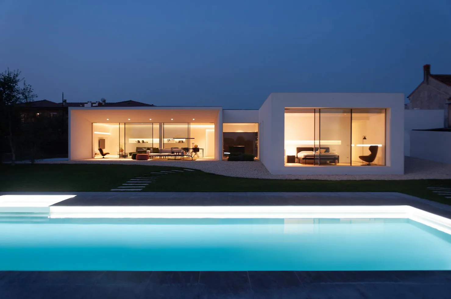 Architettura moderna di Villa MD Home a Verona, con piscina illuminata in primo piano e ampie vetrate che rivelano gli interni minimalisti. Design esclusivo di Federico Cappellina & Partners Architects