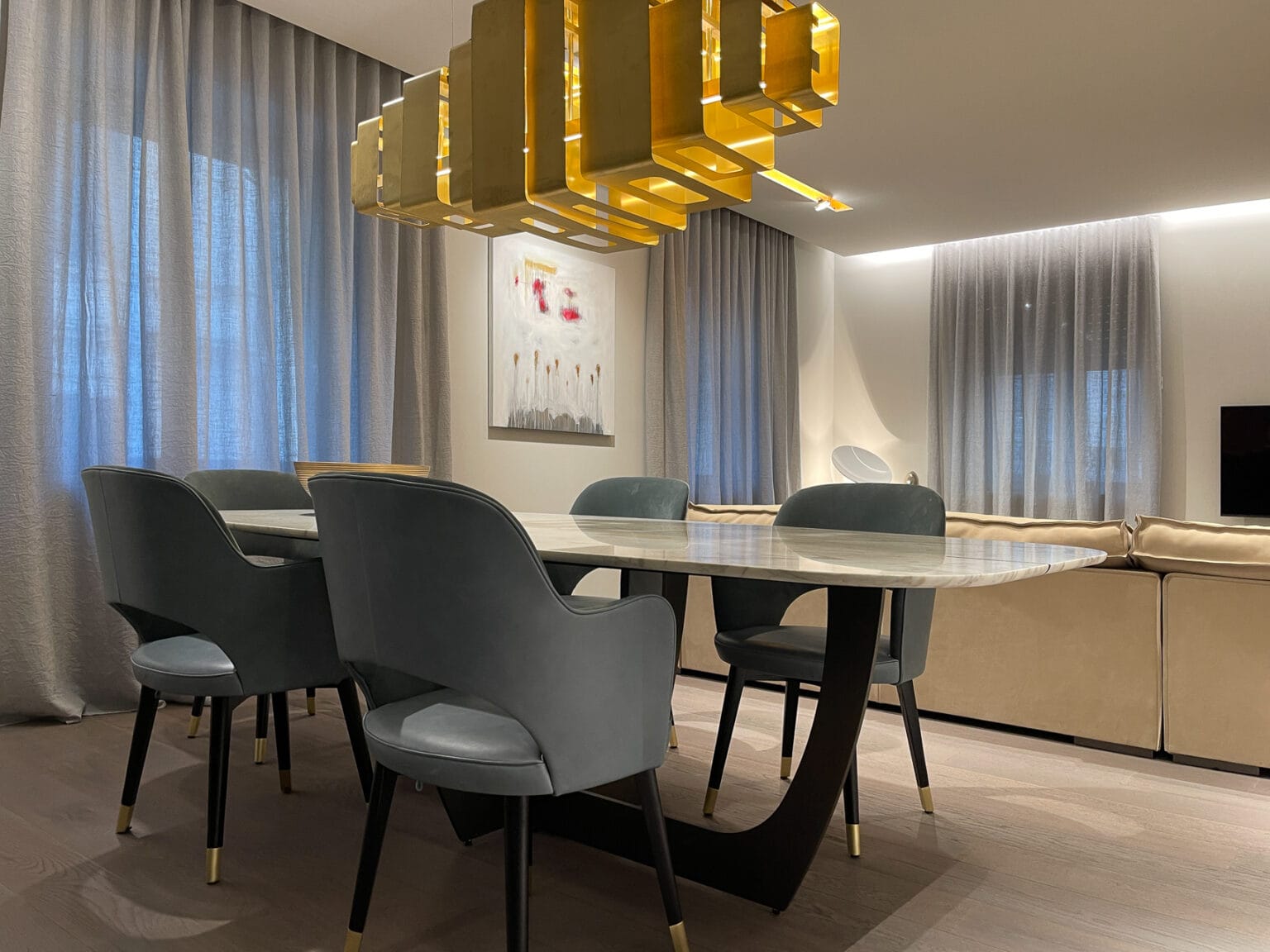 Sala da pranzo di design a Verona: tavolo in marmo, sedie imbottite grigie, e illuminazione a sospensione dorata per un ambiente lussuoso