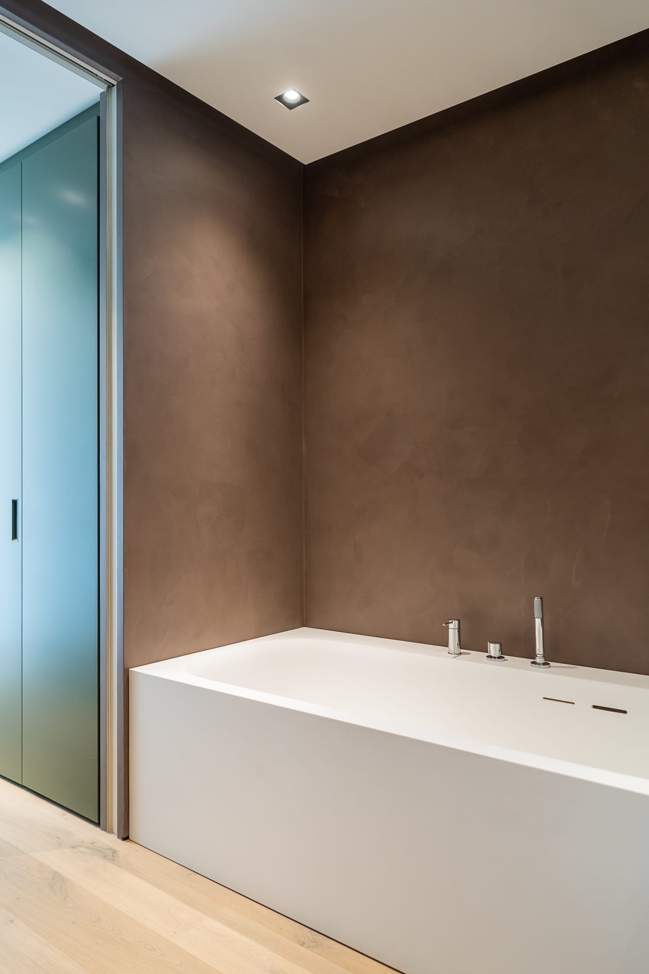Bagno moderno a Villa MD Home, Verona, con vasca rettangolare, parete marrone in stucco veneziano e pavimento in legno chiaro. Design di lusso firmato Federico Cappellina & Partners Architects