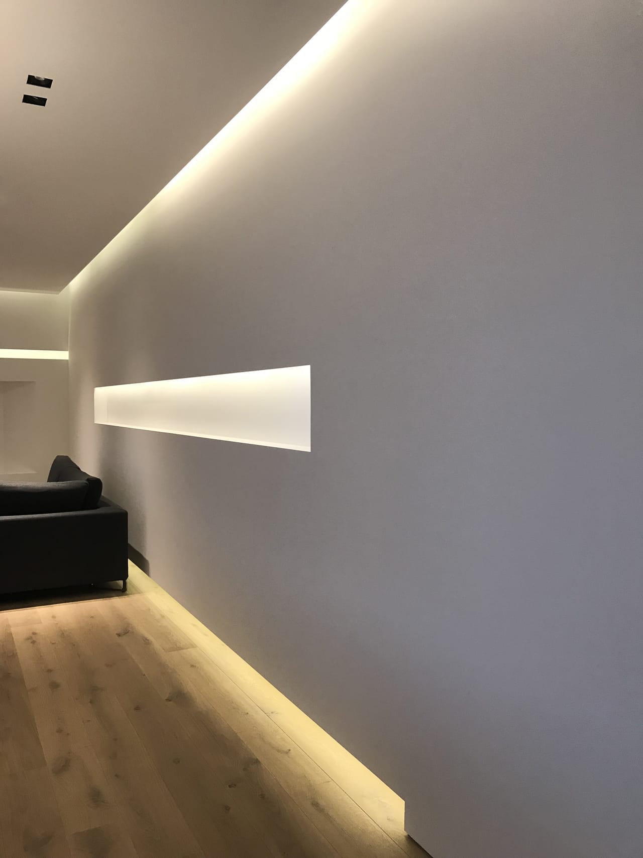 Interni minimalisti a Villa MD Home, Verona, con illuminazione a gola che definisce volumi e superfici, parquet in legno chiaro e divano moderno. Il design pulito e l'attenzione ai dettagli riflettono l'architettura contemporanea di Federico Cappellina & Partners Architects