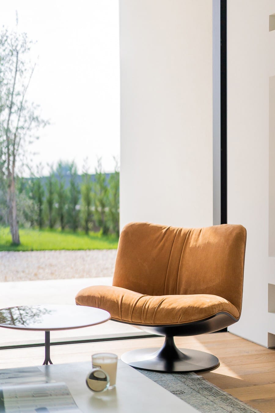 Interni di design a Villa MD Home, Verona, con poltrona in velluto color ocra, tavolino rotondo e vista sul giardino. L'illuminazione naturale e il design degli interni riflettono l'architettura contemporanea di Federico Cappellina & Partners Architects