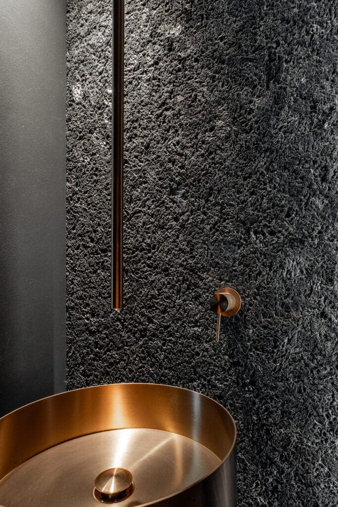 Black textured wall with copper basin and fixtures in contemporary interior design.